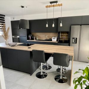 Îlot central d’une cuisine minimaliste noire avec un plan de travail et une crédence en bois, combinant élégance et chaleur naturelle.