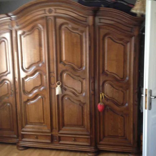 armoire ancienne en chêne massif installée dans une chambre à coucher avec portes sculptées et finitions traditionnelles