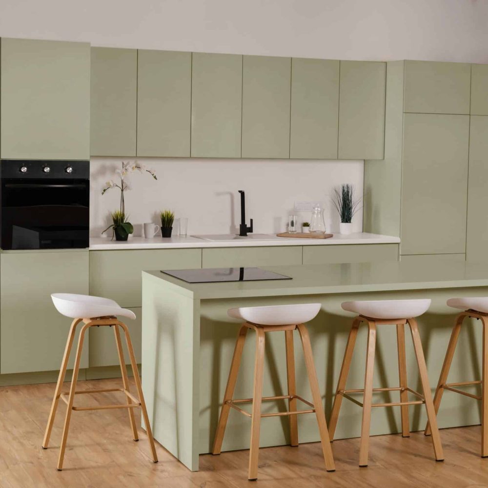 Cuisine scandinave verte avec tabourets blanc et bois clair autour ilot cuisson, crédence et plan de travail blanc sol parquet clair